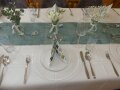 gedeckter Tisch mit Serviette, Vase mit weißen Blumen und Eukalyptusblätter und blauem Tischläufer