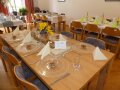 gedeckter Tisch mit Blumengesteck mit Sonnenblume, Salzbrezeln in Glasschüssel, Weizenähren und cremefarbenen Servietten
