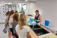 Das Foto zeigt die Fachschülerinnen Maria Sinning und Anna-Maria Wiedemann mit einer Gruppe Schülerinnen. Anna-Maria Wiedemann führt vor, welche Schritte bei der Schuhreinigung wichtig sind.