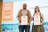 Zwei Personen mit Urkunden vor einer Leinwand