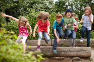 Kinder sprigen über einen Holzstamm. 